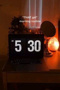 a laptop computer sitting on top of a wooden desk next to a clock and lamp