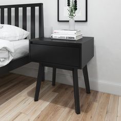 a nightstand with two books and a plant on it next to a bed in a white room