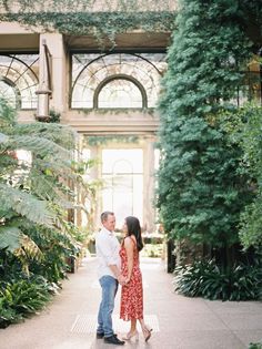 an engaged couple standing in the middle of a walkway surrounded by plants and greenery