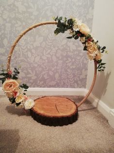 a wooden circle with flowers and greenery around it on carpeted floor next to wall