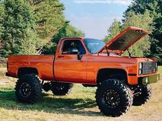 an orange pick up truck with its hood open in the middle of a grassy field