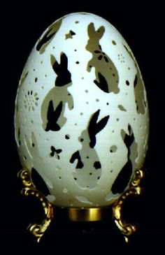 an egg with black and white designs on it sitting on a gold stand in front of a black background