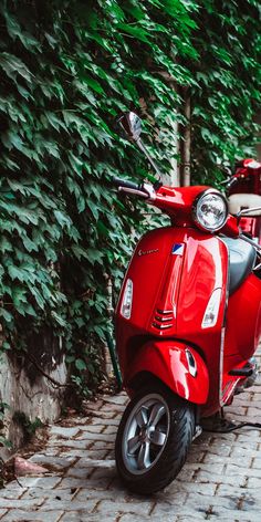 a red scooter parked on the side of a brick road next to trees