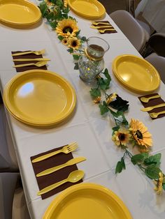 the table is set with yellow plates and sunflowers on each plate, along with place settings