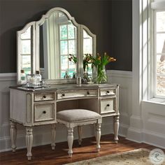 a white vanity with mirror and stool in front of it next to a large window