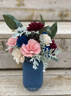 a blue mason jar filled with flowers on top of a wooden table next to a bench