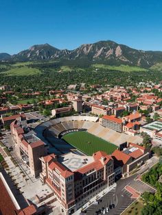 an aerial view of a baseball stadium and surrounding buildings with mountains in the back ground