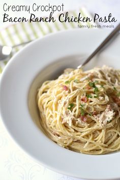 a white bowl filled with pasta and meat on top of a table next to a fork