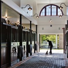 a person is cleaning the floor in front of several stalls with horse stalls on either side