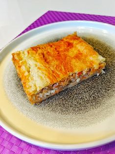 a piece of food sitting on top of a white plate next to a purple place mat