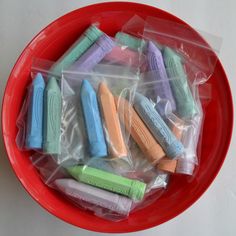 a red bowl filled with lots of different colored crayons in plastic wrappers