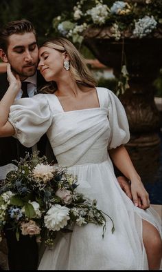 a man and woman sitting next to each other in front of a fountain with flowers