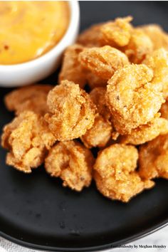 some fried food on a black plate next to a bowl of dip and dipping sauce