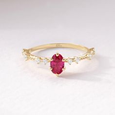 a yellow gold ring with an oval shaped ruby stone surrounded by small white diamond accents