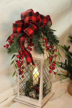 a lantern with a red and black plaid bow on it sitting next to a christmas tree