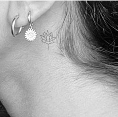 the back of a woman's ear has a small flower tattoo on it