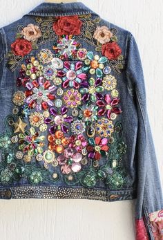 a denim jacket with flowers on it hanging from a hook in front of a white wall