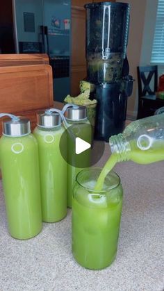 a person pouring green liquid into four glasses on a counter top next to a blender