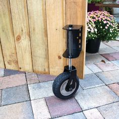 a black scooter sitting on top of a brick floor next to a wooden fence