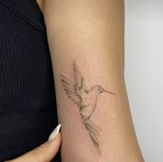 a woman's arm with a small tattoo of a hummingbird on the left side