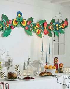 a table topped with lots of food next to a wall covered in paper flowers and candles