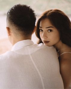 a man and woman sitting next to each other in front of a window looking at each other