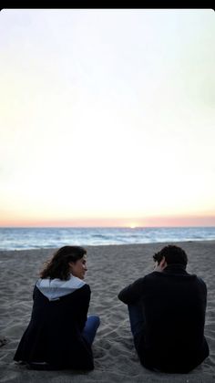 two people sitting on the sand at the beach