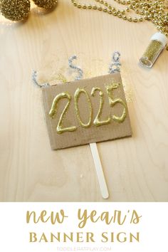 a new year's banner sign on a wooden table with gold glitter and decorations