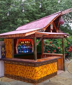 an outdoor bar with lots of bottles on the outside and lights hanging from the roof