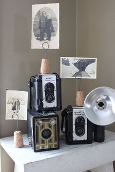 three old fashioned cameras sitting on top of a white table next to a silver object