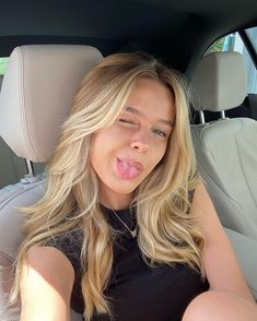 a woman sticking her tongue out in the back seat of a car while sitting down