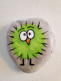 a rock with a green bird painted on it's face and eyes, sitting next to a white wall