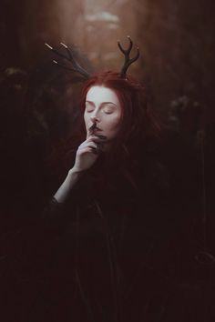 a woman with red hair and antlers on her head is sitting in the dark