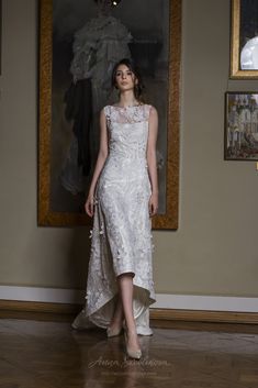 a woman standing in front of a painting wearing a white dress