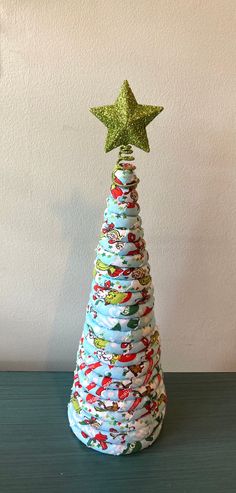 a christmas tree made out of wrapping paper with a gold star on top, sitting on a table in front of a white wall