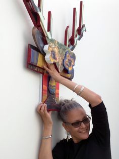 a woman is holding up some kind of art piece on the side of a wall