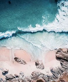 an aerial view of the beach and ocean with waves coming in from the rocks on the shore