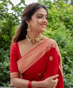 a woman in a red sari with gold jewelry on her neck and shoulder, smiling