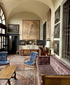 a living room filled with lots of furniture and paintings on the wall next to windows