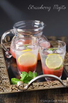 two glasses filled with red liquid and lemon slices on a tray next to a pitcher