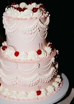 a three tiered cake with cherries on the top is pink and has white icing