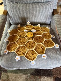 a crocheted bee sitting on top of a gray chair with white daisies