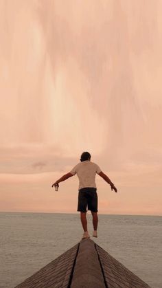 a man standing on top of a wooden pier next to the ocean with his arms outstretched