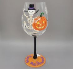 a wine glass with a skeleton on it and a pumpkin in the middle, sitting on top of an orange coaster