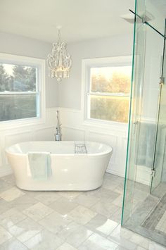 a white bath tub sitting in a bathroom next to two windows and a chandelier