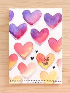 a card with watercolor hearts and the words love you written on it in different colors