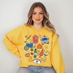 a woman wearing a yellow sweatshirt with various items on it and smiling at the camera