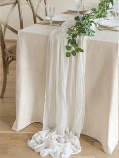 the table is set with white linens and greenery