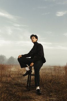 a man sitting on top of a stool in a field