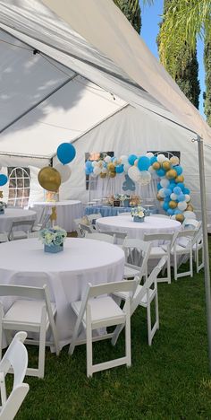 tables and chairs are set up under a tent for an outdoor party with blue, gold and white balloons